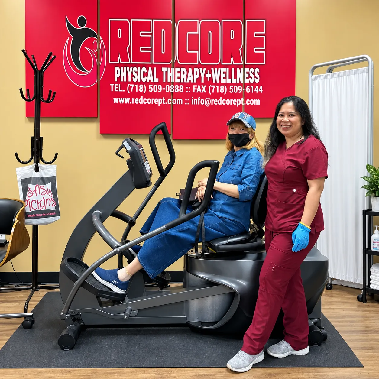 A RedCore clinician in maroon scrubs standing beside a patient using a seated elliptical, under the RedCore sign.
